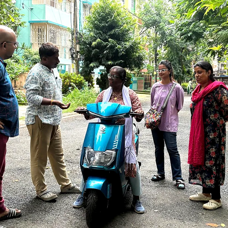 Older woman learning to ride a scooty while her family watches